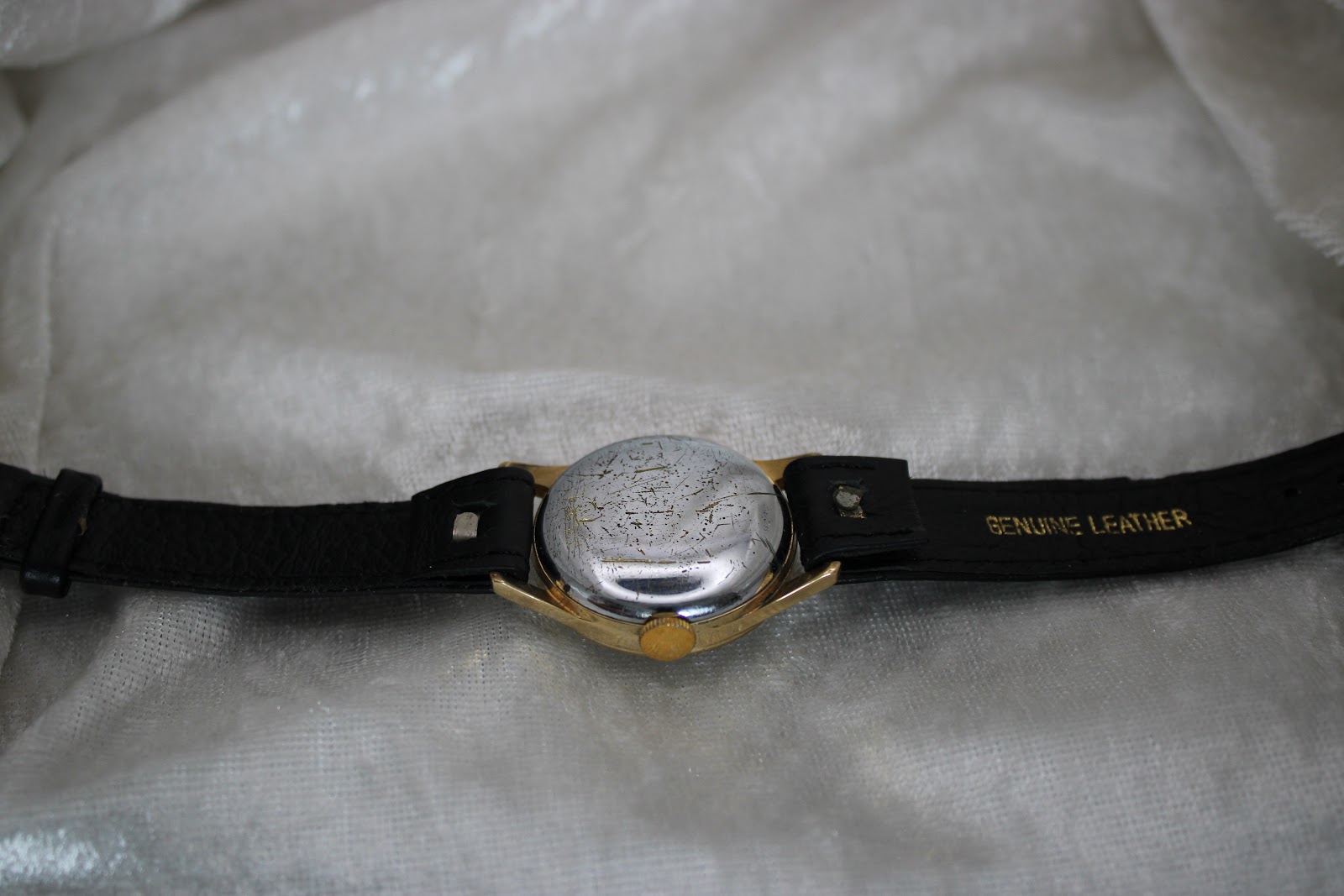 Wider view of the watch's case back and the attached black leather strap, which has 'GENUINE LEATHER' embossed on the underside.