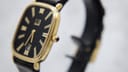 Angled side view of the Dunhill watch, highlighting the gold-toned case, black dial, and crown with a black cabochon.