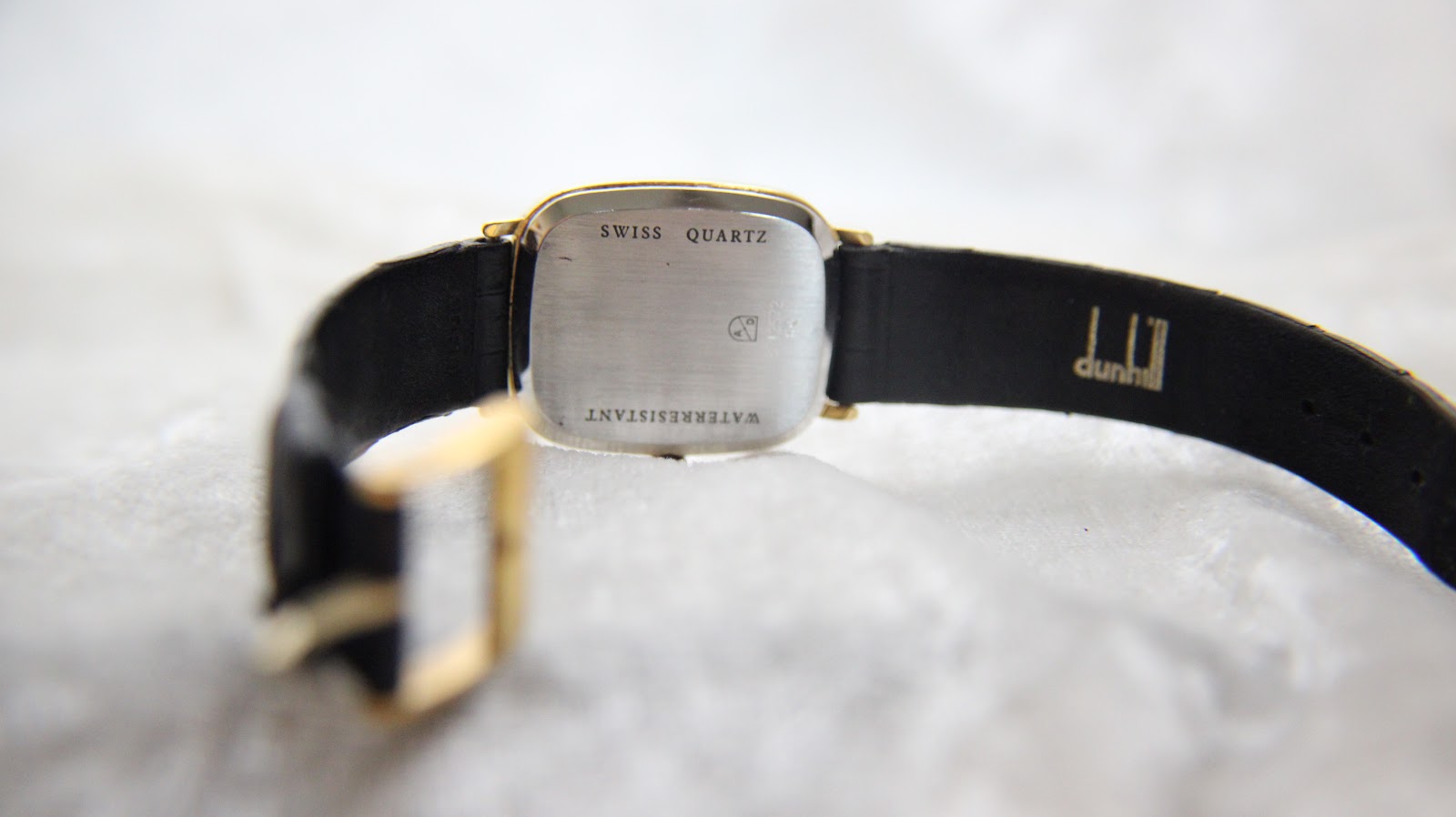 Another view of the case back and black leather strap, showing "SWISS QUARTZ" and "dunhill" signature on the strap.