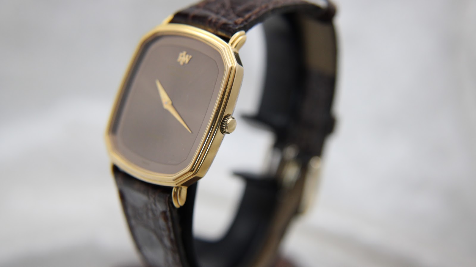 Angled side view of the Raymond Weil watch showing the gold case, crown, and brown crocodile-pattern leather strap.