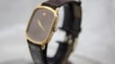 Angled side view of the Raymond Weil watch showing the gold case, crown, and brown crocodile-pattern leather strap.