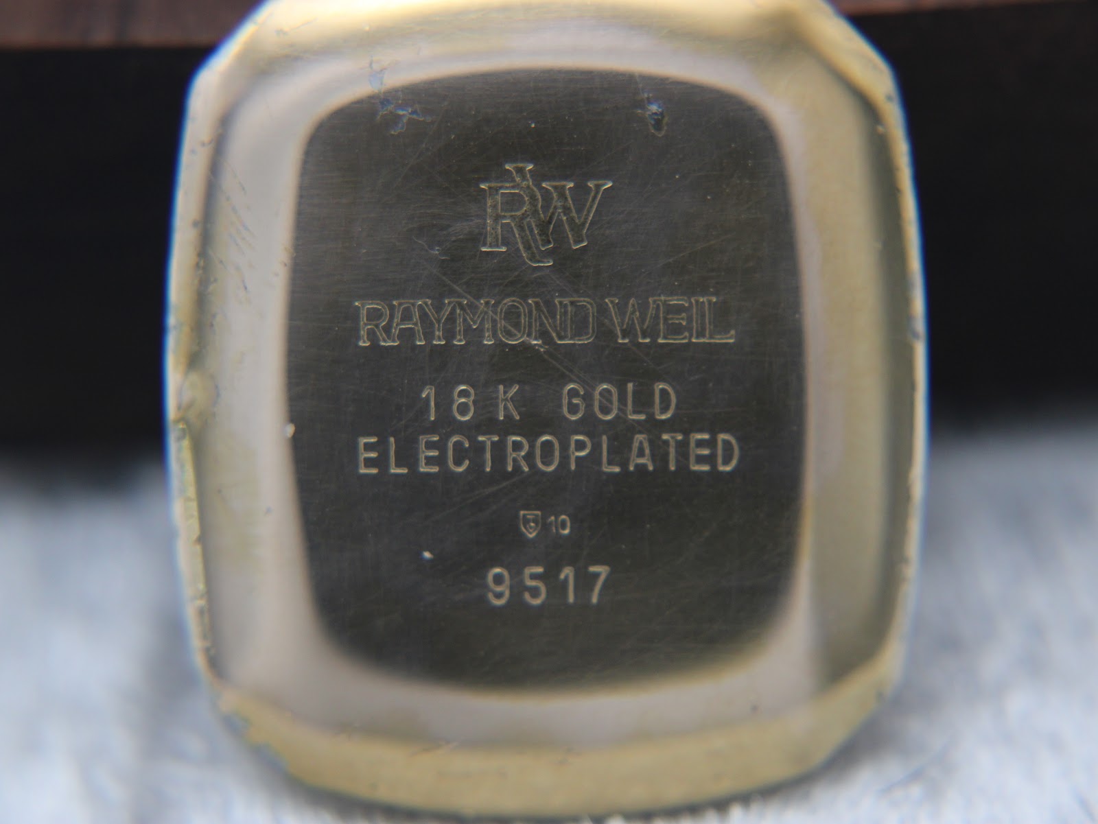 Close-up of the watch case back, clearly showing 'RW Raymond Weil 18K GOLD ELECTROPLATED 9517' engraving.