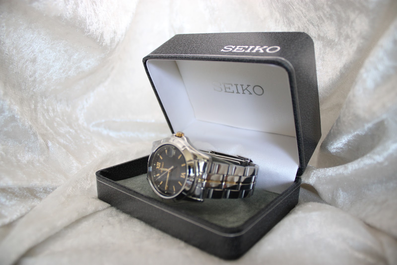 Angled view of the Seiko perpetual calendar watch placed inside its original black Seiko presentation box on a white fabric background.