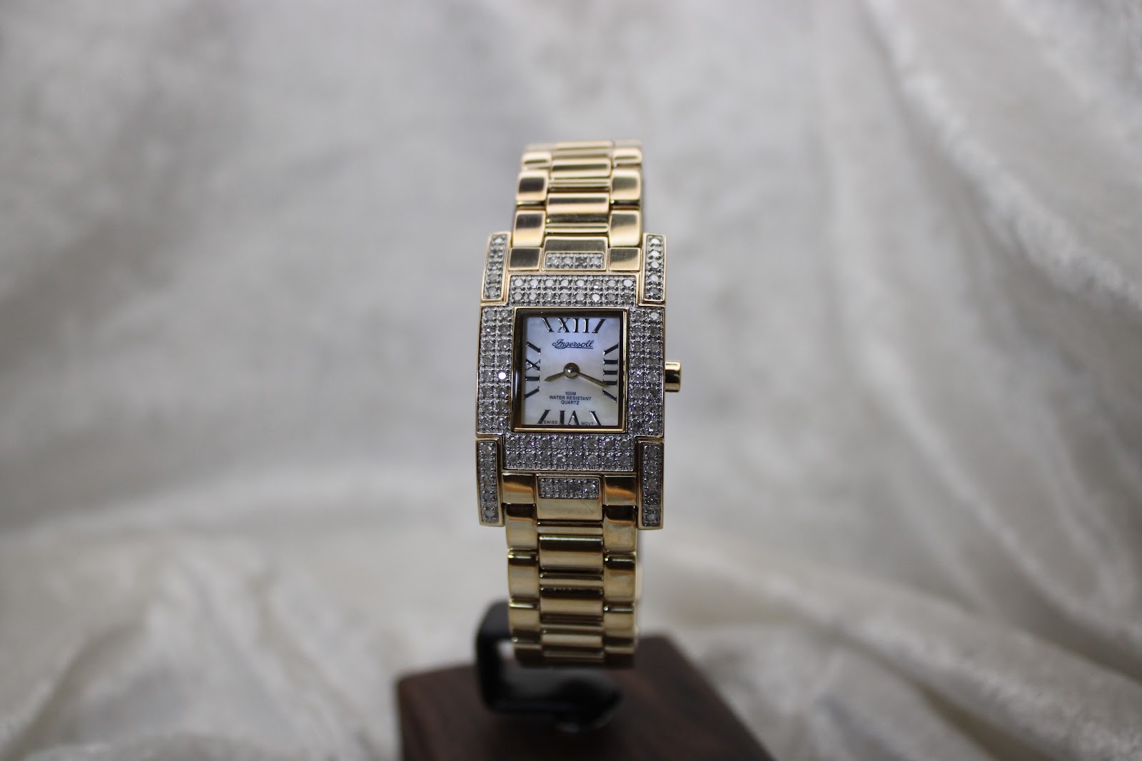 Full front view of the Ingersoll Diamond watch with its gold-tone bracelet displayed on a black stand.