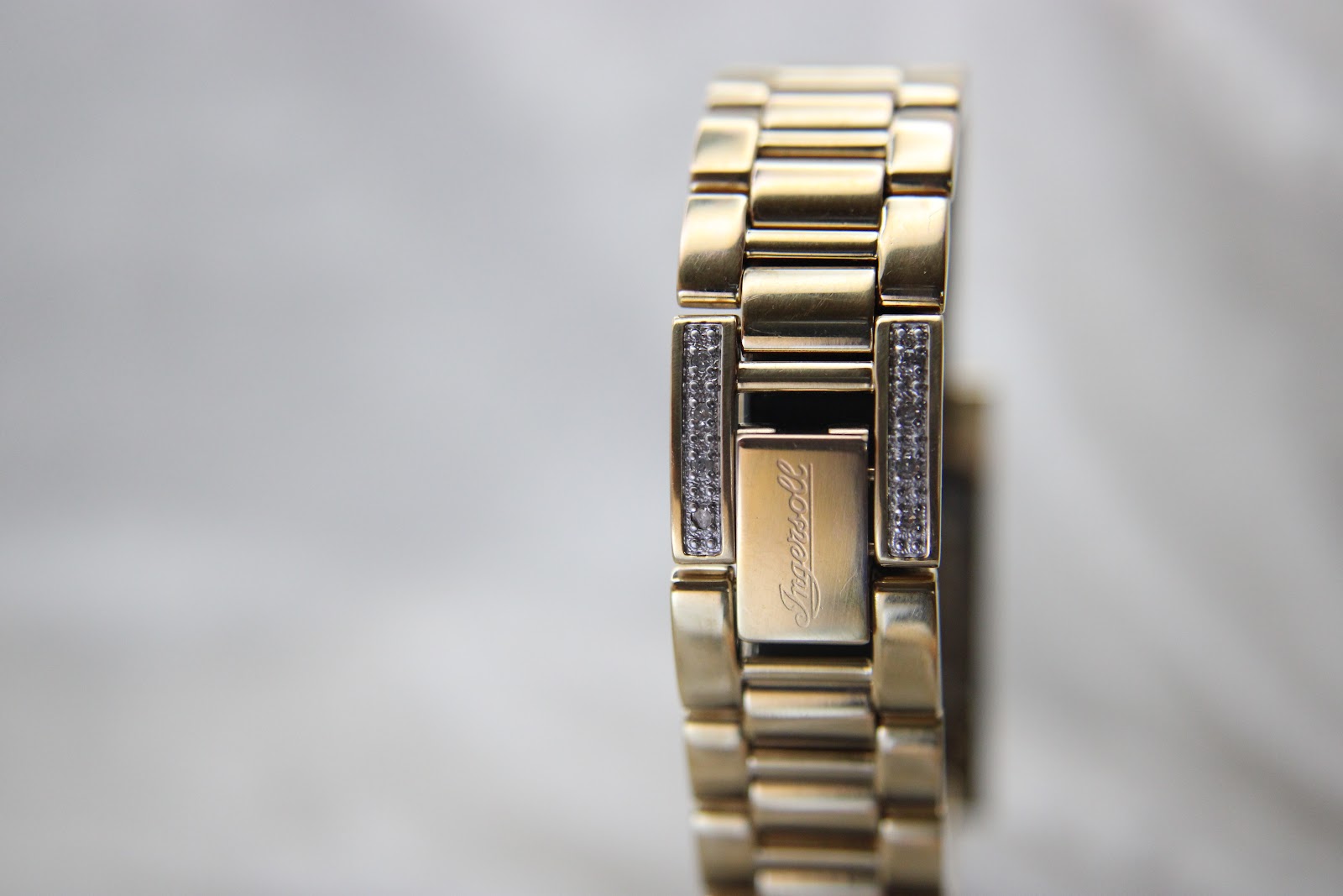 Close-up of the gold-tone bracelet and the signed Ingersoll deployment clasp, adorned with crystal details.