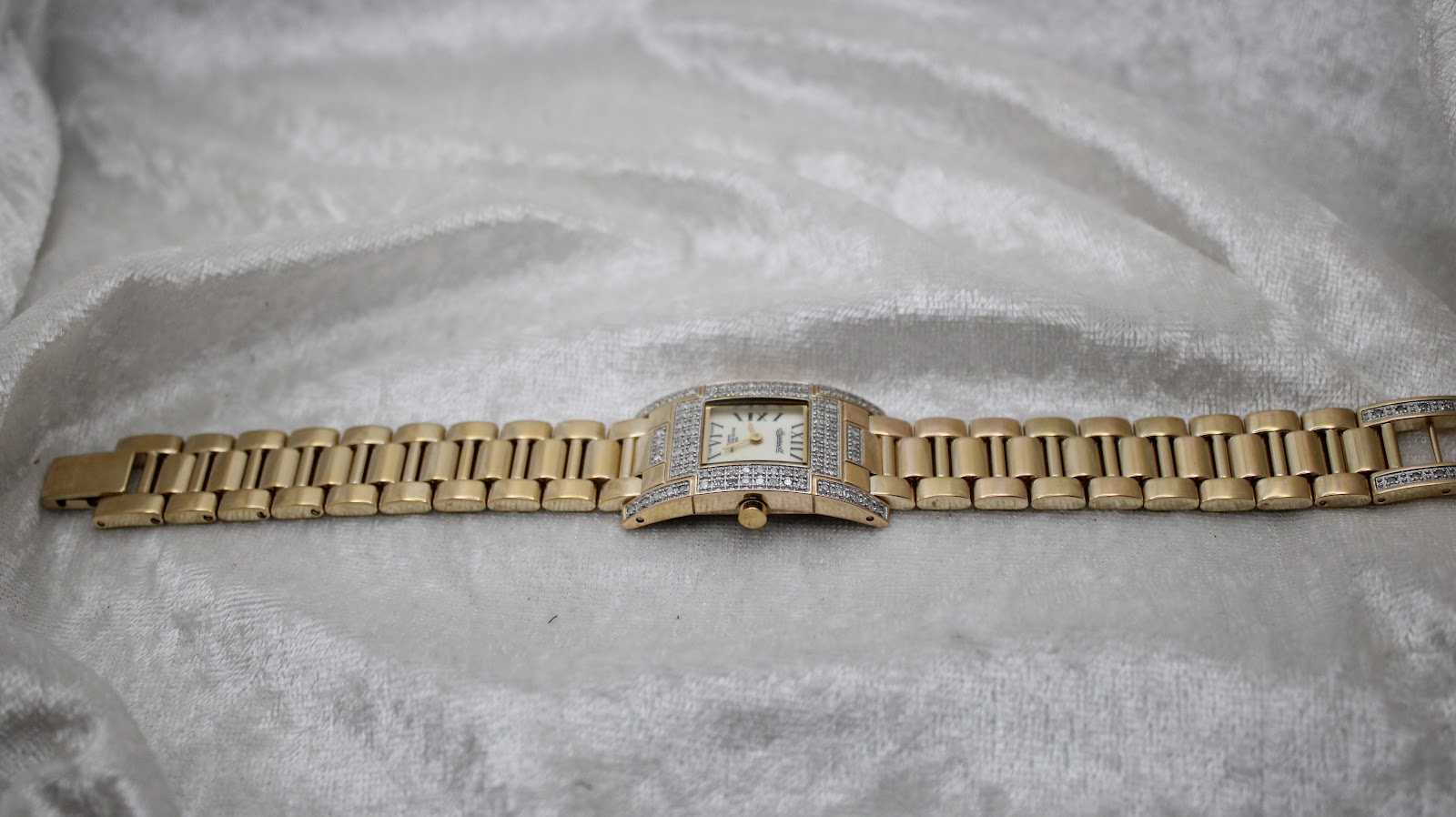 Overhead view of the Ingersoll Diamond watch with its gold-tone bracelet fully extended on a white textured surface.