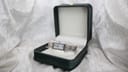 Maurice Lacroix two-tone rectangular watch presented open in a dark green box on a white textured surface.