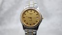 Front view of the Tissot PR 50 gold-tone dial, showing applied gold baton hour markers, a date window at 3 o'clock, and the Tissot logo.