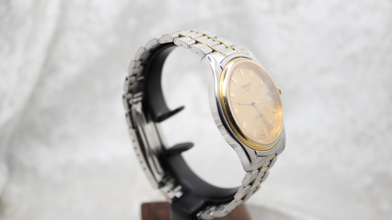 Another angled view of the Tissot PR 50 on a black display stand, highlighting the watch's profile and bi-metal bracelet from the left.