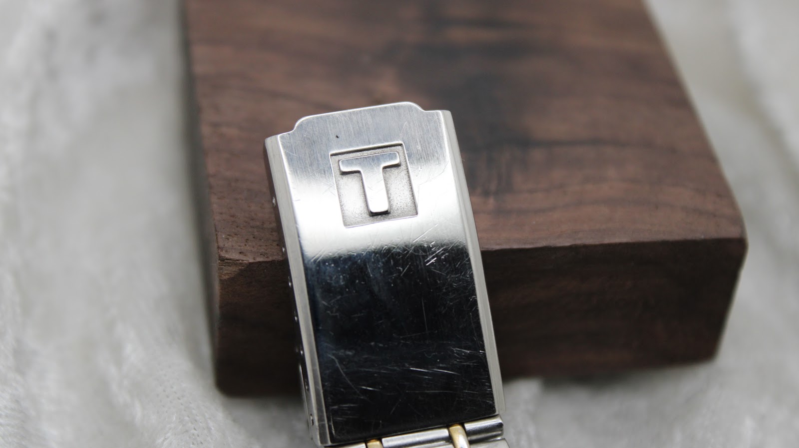 Close-up of the polished bi-metal bracelet clasp, featuring the engraved Tissot 'T' logo.