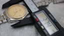 Digital caliper measuring the Tissot PR 50 case diameter at 37.4mm, with the gold-tone dial partially visible in the background.