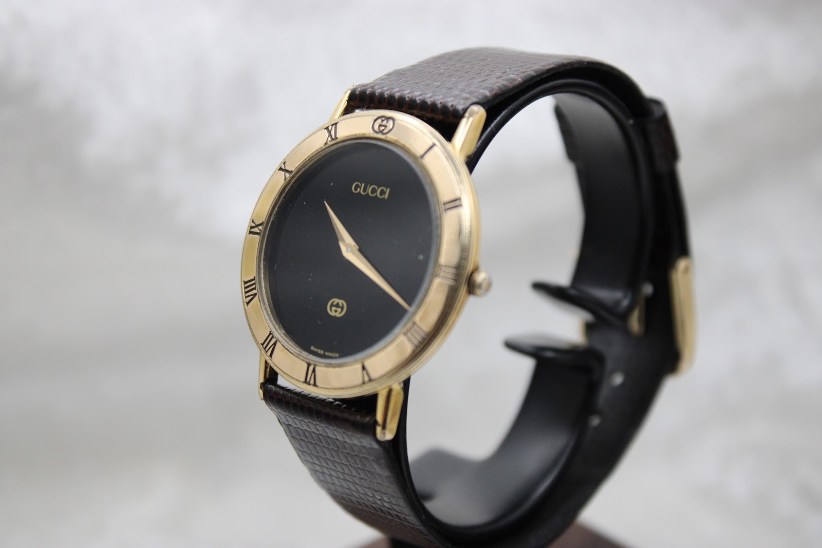 The Gucci 3000M watch displayed on a stand, angled front view, showcasing its presence.