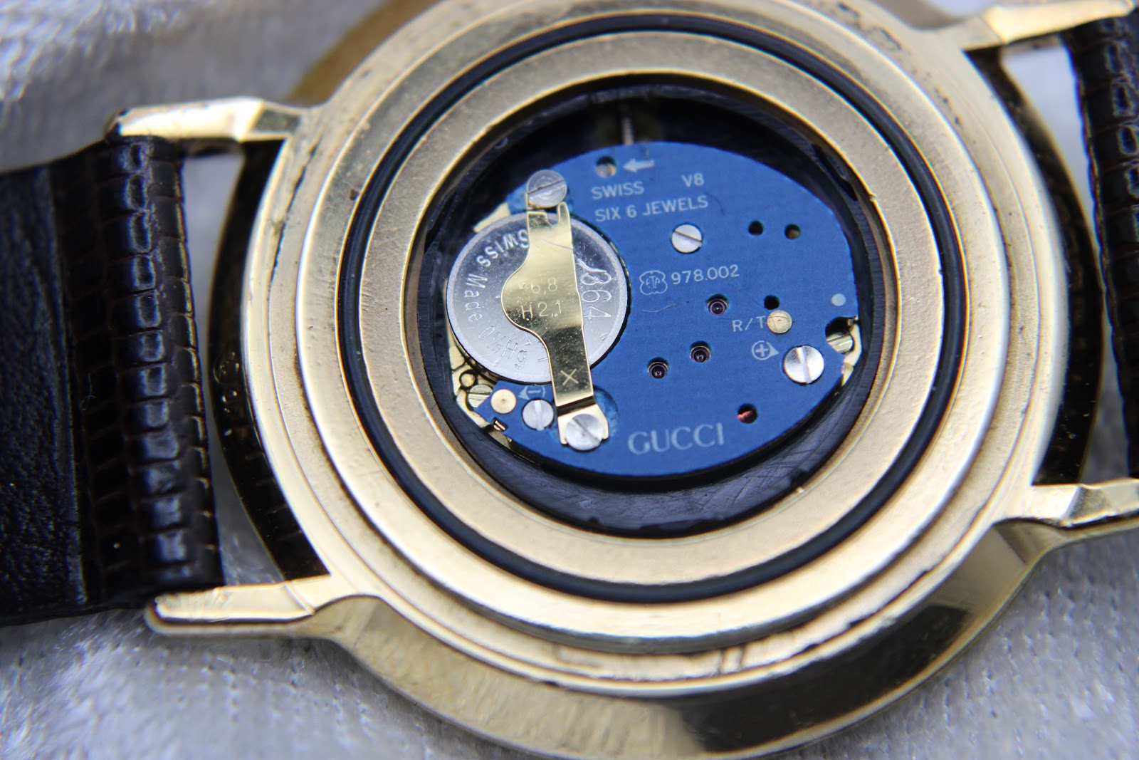 Close-up of the opened case back revealing the blue Swiss V8 quartz movement with six jewels and battery.