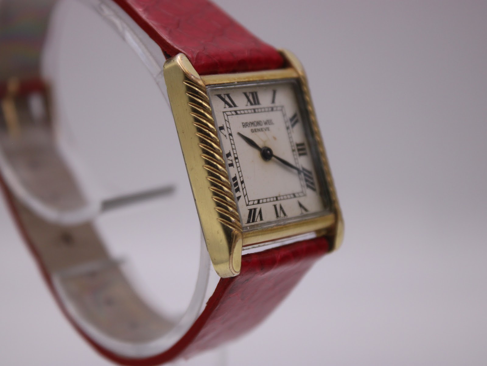 Direct front view of the rectangular Raymond Weil Genève watch, showcasing its cream dial with black Roman numeral indices and hands, framed by the gold-tone case.