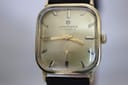 Front view of gold-tone Junghans watch dial with champagne face, gold baton indices and hands, and a sub-seconds dial.