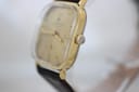 Angled side view of the gold-tone Junghans watch showing the crown and curved acrylic crystal.