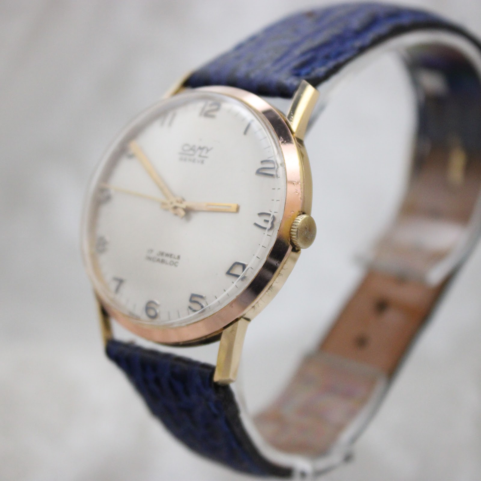 Close-up angled view of the watch crown and case side, showing the texture of the navy blue strap and some minor wear on the gold plating.