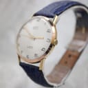 Close-up angled view of the watch crown and case side, showing the texture of the navy blue strap and some minor wear on the gold plating.