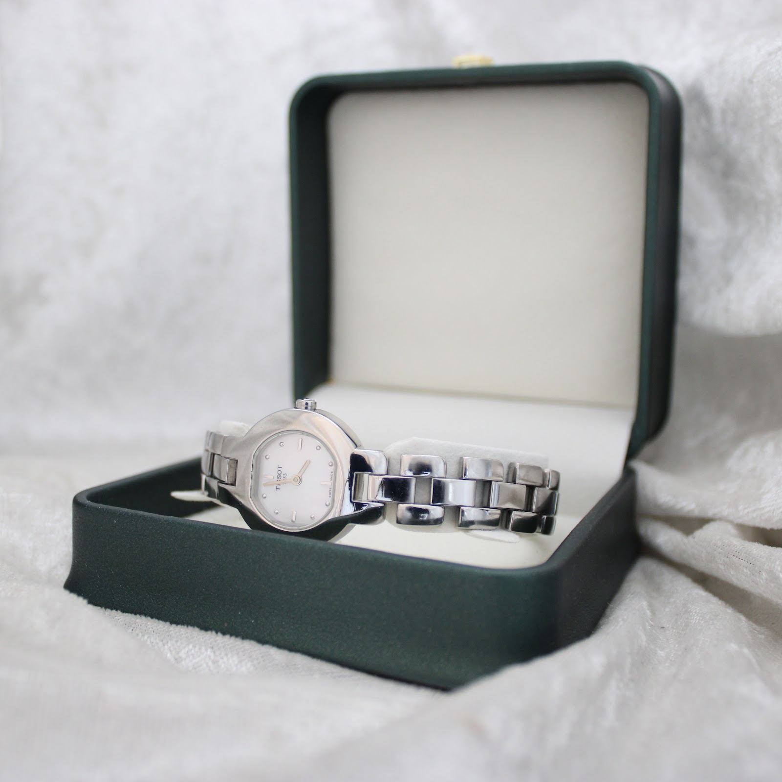 Tissot G330 watch with silver-tone case and bracelet, presented in an open dark green watch box.
