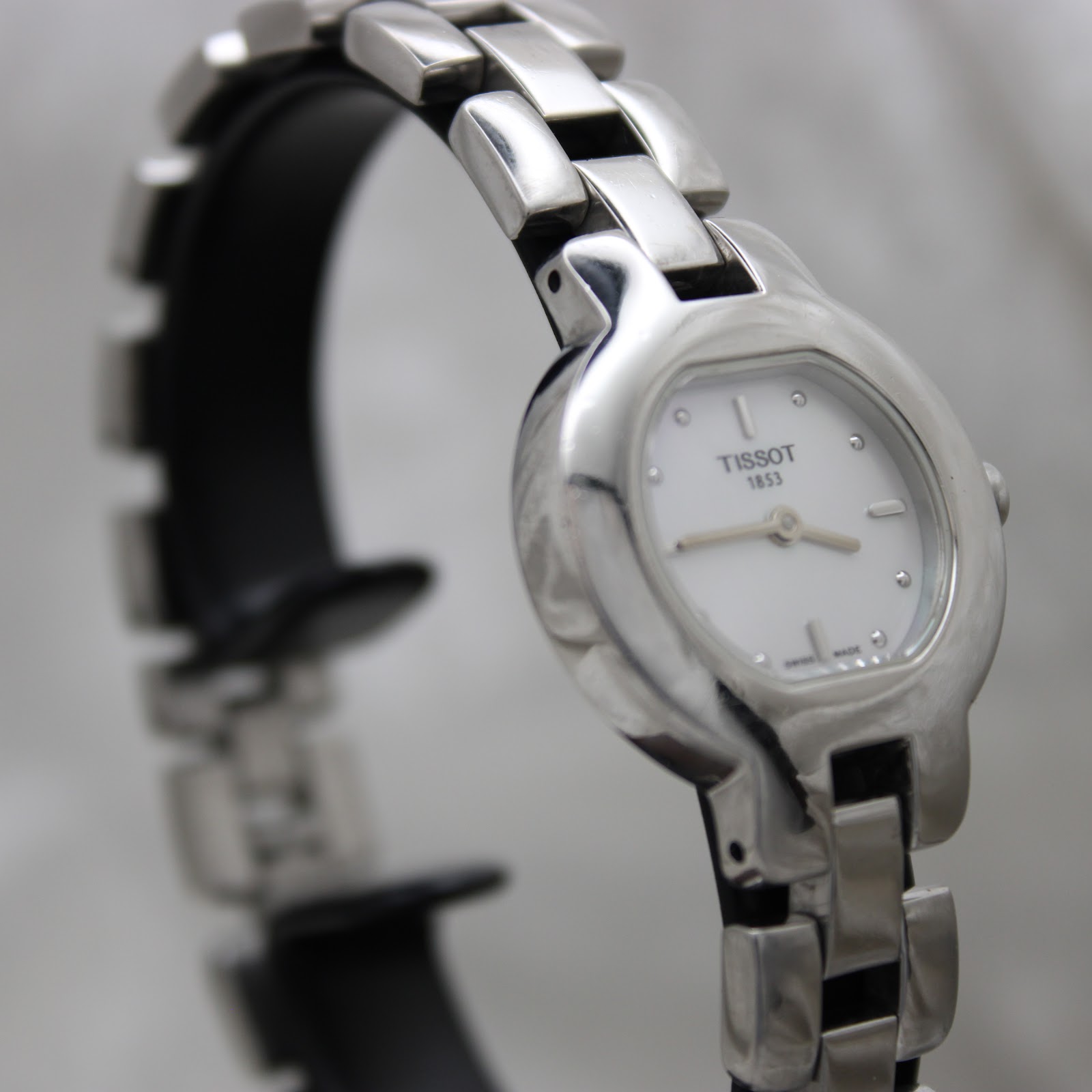 Angled close-up of the Tissot G330 watch on a black stand, highlighting the polished stainless steel case and bracelet.