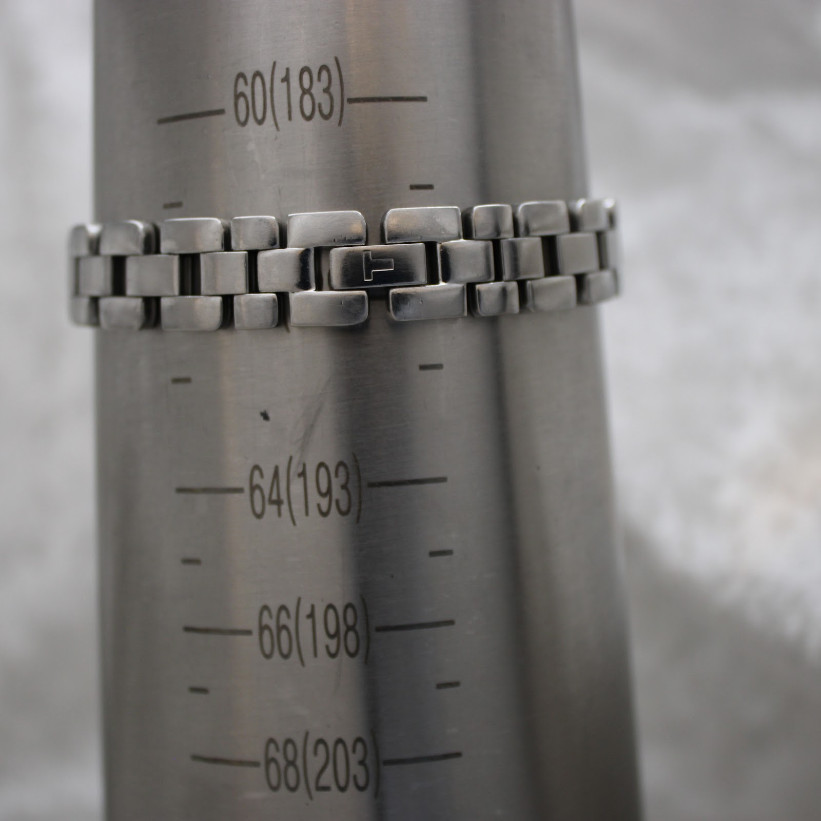 Close-up of the Tissot G330's integrated bracelet and signed butterfly clasp on a wrist sizing gauge, indicating a fit of 183mm.