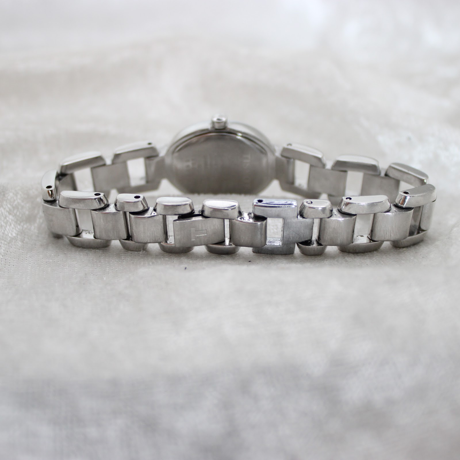Rear view of the integrated stainless steel bracelet and hidden clasp of the Tissot G332 watch, laid flat on a white textured surface.