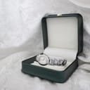 The Tissot G332 watch resting inside an open dark green presentation box with cream interior, set against a soft white textured background.