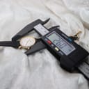 Overhead view of the Tissot T852K watch case being measured by a digital caliper, displaying a precise diameter of 26.0mm.