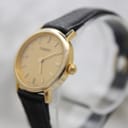 Angled view of the Tissot watch, showing the gold-plated case, crown, champagne dial, and black leather strap from the right side.