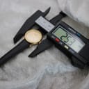 Tissot watch laid next to a digital caliper displaying a measurement of 25.3 mm, indicating the total width of the watch including the crown.