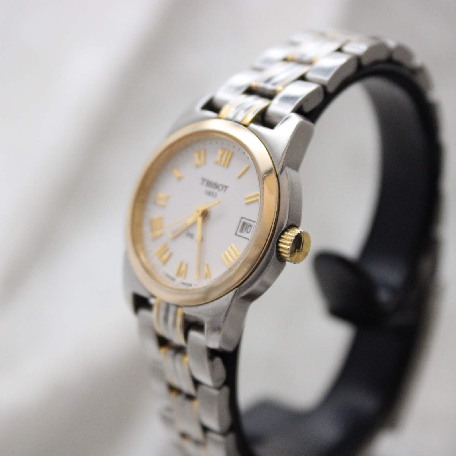 Angled view of the Tissot PR 50 watch showing the gold-tone bezel and crown on a watch stand.