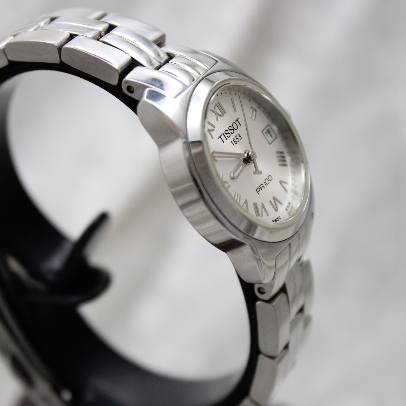 Close-up of the Tissot PR 100 stainless steel bracelet and signed clasp.