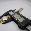 Close-up of a digital caliper measuring the case size of the Tissot watch at 21.4mm, with the watch lying on a white surface.