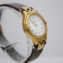 Another angled side view of the Tissot Stylist watch, focusing on the curved gold-tone case and textured brown strap.