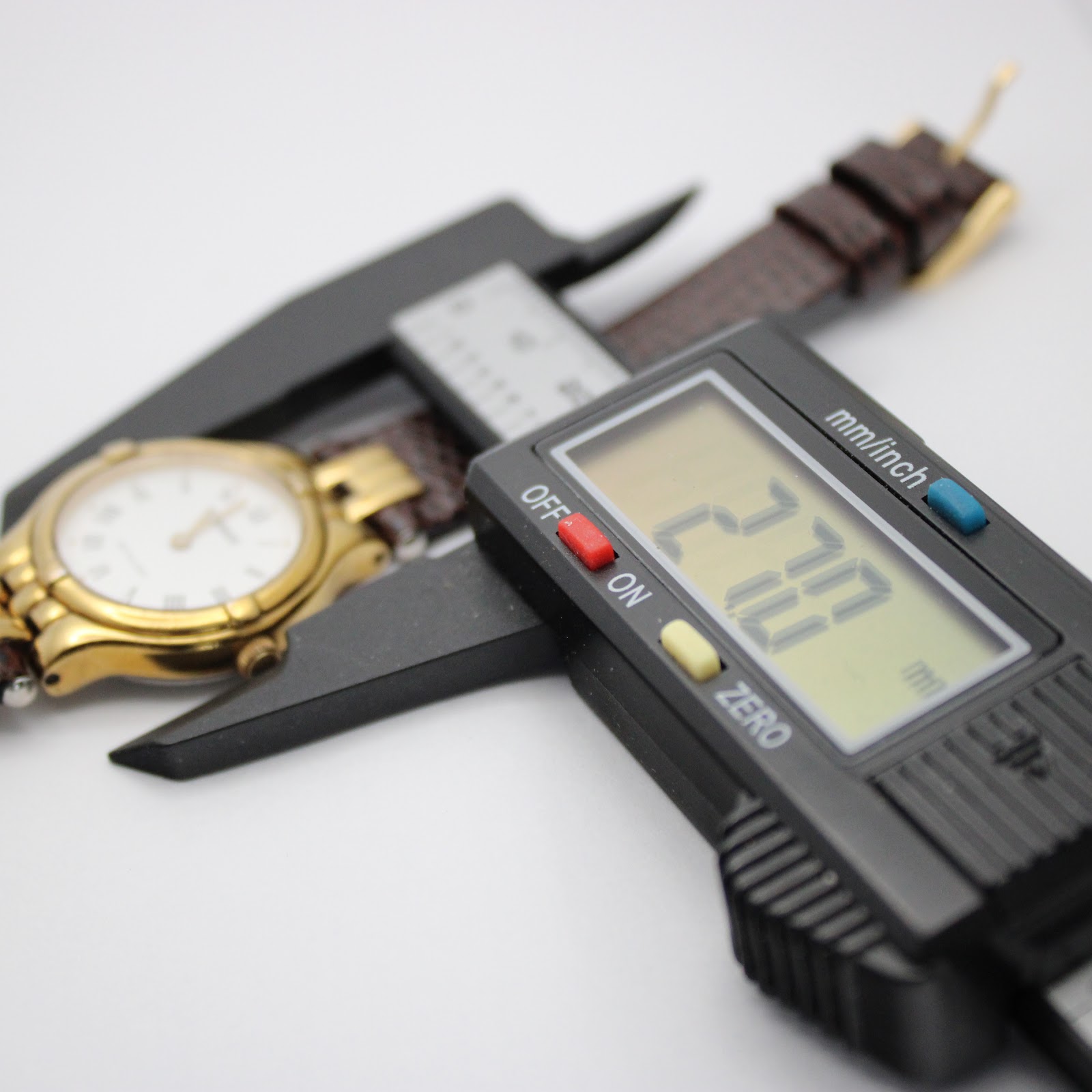 Top-down view of the watch being measured by a digital caliper, displaying 27.70 mm for the case diameter.