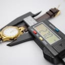 Top-down view of the watch being measured by a digital caliper, displaying 27.70 mm for the case diameter.