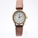 Front view of the Tissot women's quartz watch, showing its round gold-tone case, white dial with black Arabic numerals, and brown leather strap on a stand.