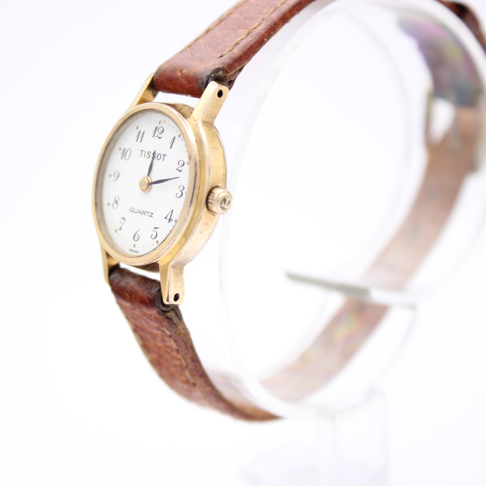 Angled side view of the Tissot quartz watch, highlighting the gold-tone case, polished bezel, and the watch's slim profile with the brown leather strap.