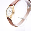 Angled side view of the Tissot quartz watch, highlighting the gold-tone case, polished bezel, and the watch's slim profile with the brown leather strap.