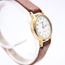 Close-up, slightly elevated angled view of the Tissot watch, focusing on the white dial, slender hour and minute hands, and the texture of the brown leather strap.