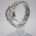Angled side view of the Tissot 1853 watch on a clear display stand, highlighting the two-tone bracelet and gold-tone crown.