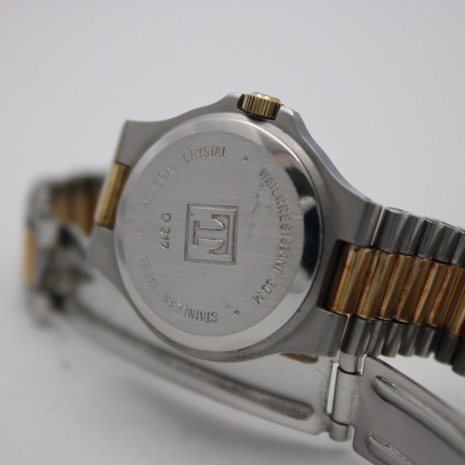 Close-up of the watch case back, revealing "TISSOT", "MINERAL CRYSTAL", "WATERRESISTANT 30 M", "STAINLESS STEEL", and "D 317" engravings, with a view of the clasp.