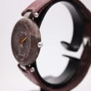 Angled side view of the Tissot Rock Watch R150, highlighting the integrated red leather strap and the natural texture of the stone case.