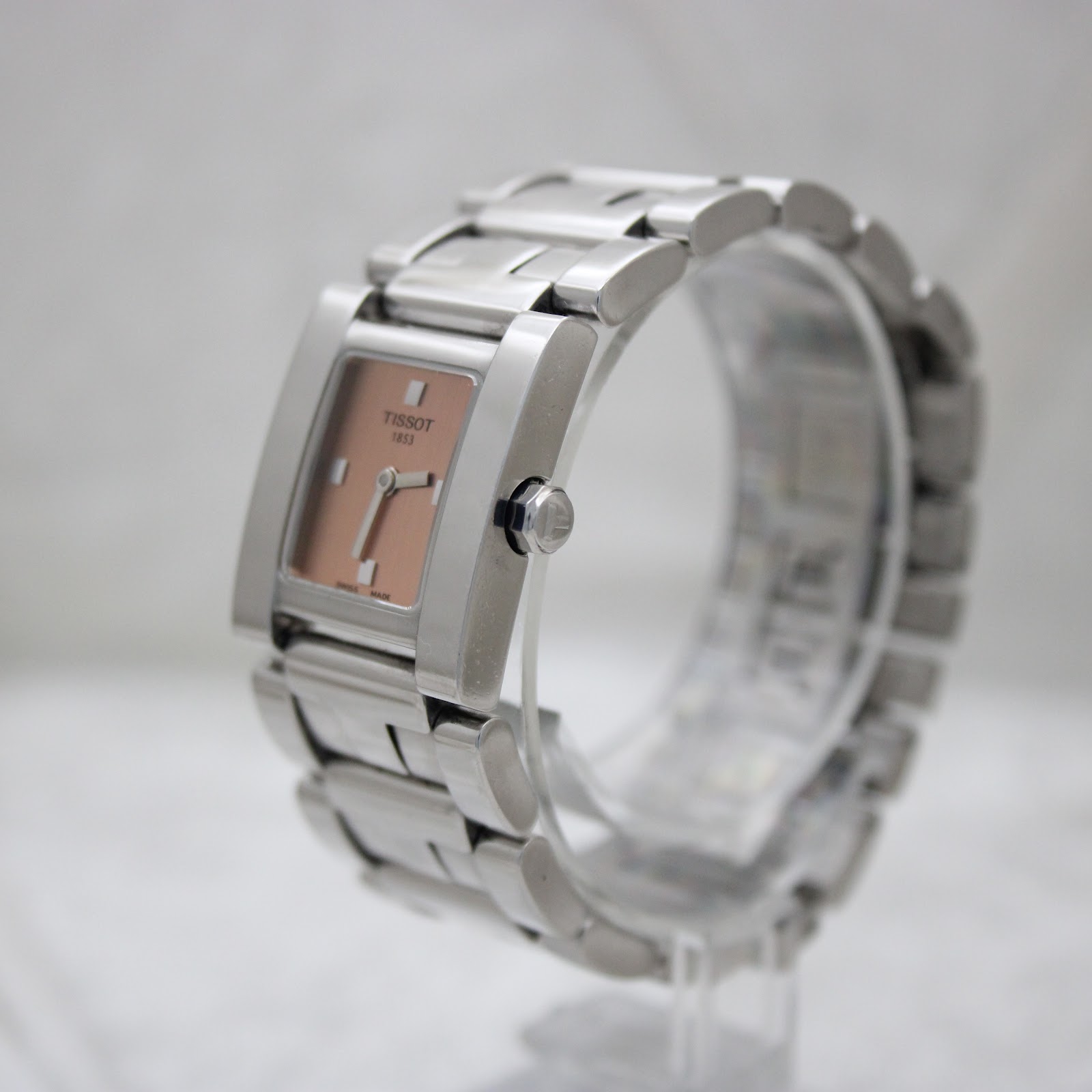 Side angle view of the Tissot square watch showing the right profile and crown, with the steel bracelet on a stand.