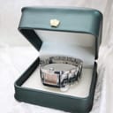 The Tissot square watch resting in an open green presentation box with a golden crown emblem, though the box is not included with the sale.