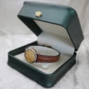 Tissot watch displayed inside an open dark green presentation box, resting on a white insert, showing the front of the watch and strap.