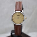 Front-facing view of the Tissot watch on a stand, clearly showing the warm cream dial with applied gold baton indices and "Tissot" logo, silver-tone bezel, and brown leather strap.