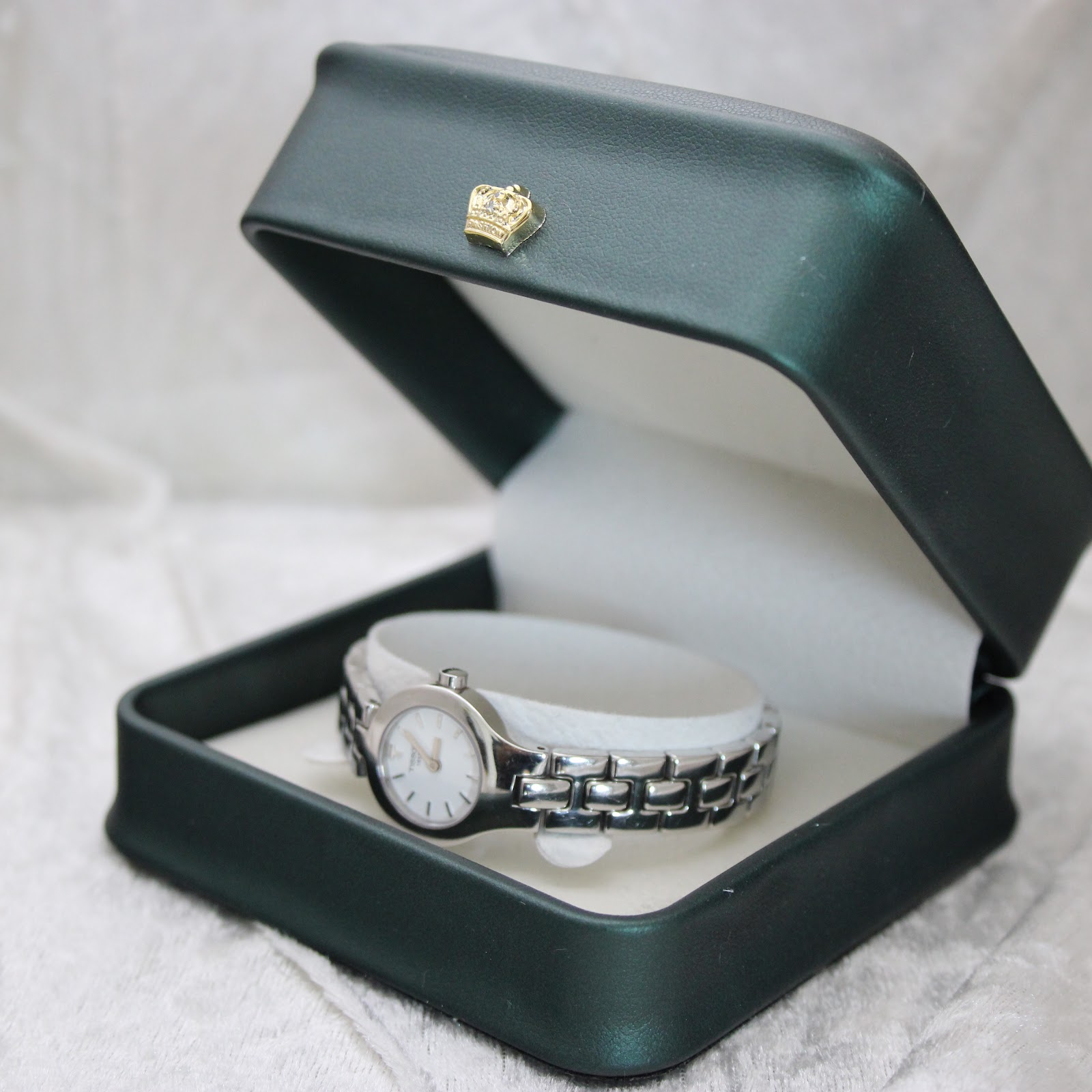 The Tissot G334 watch nested inside a dark green presentation box with a decorative gold crown emblem on the lid.