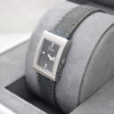 Angled view of Christian Dior D78-109 watch on grey display cushion, showing side of rectangular steel case and crown.