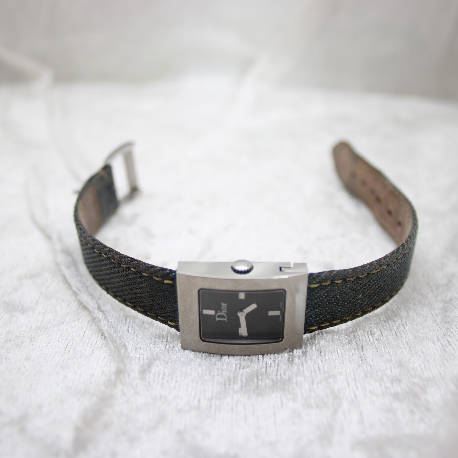 Full view of the Dior D78-109 watch with the denim strap unbuckled, on a white surface.